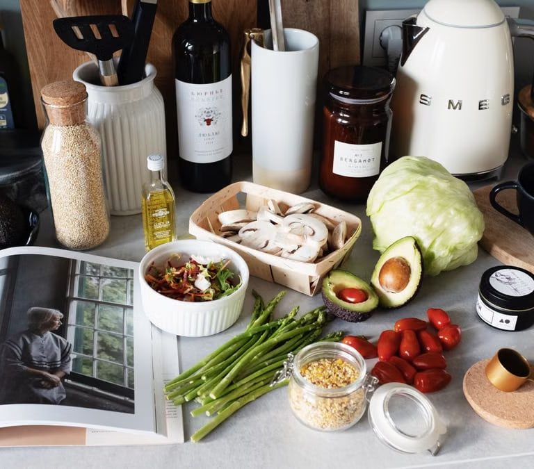 Various colorful healthy food and vegetables locating on countertop next to many different utensils and white kettle during cooking in stylish kitchen