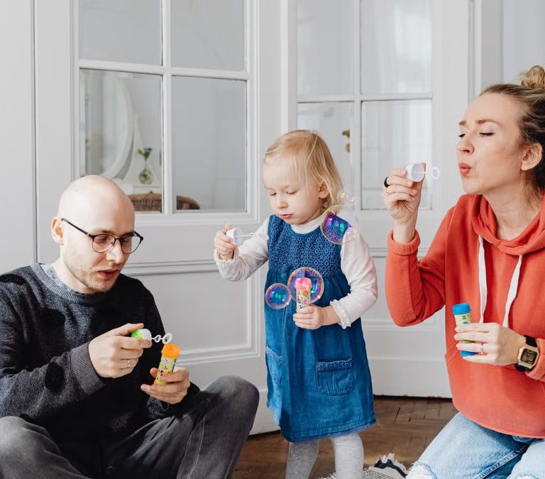 Family enjoying quality time blowing bubbles indoors, capturing joyful moments.
