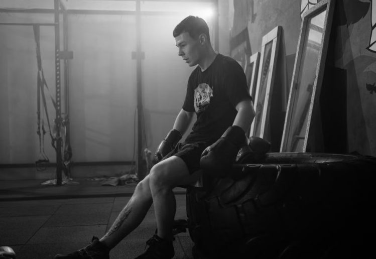 Black and white photo of a boxer resting indoors, showcasing mood and fitness.