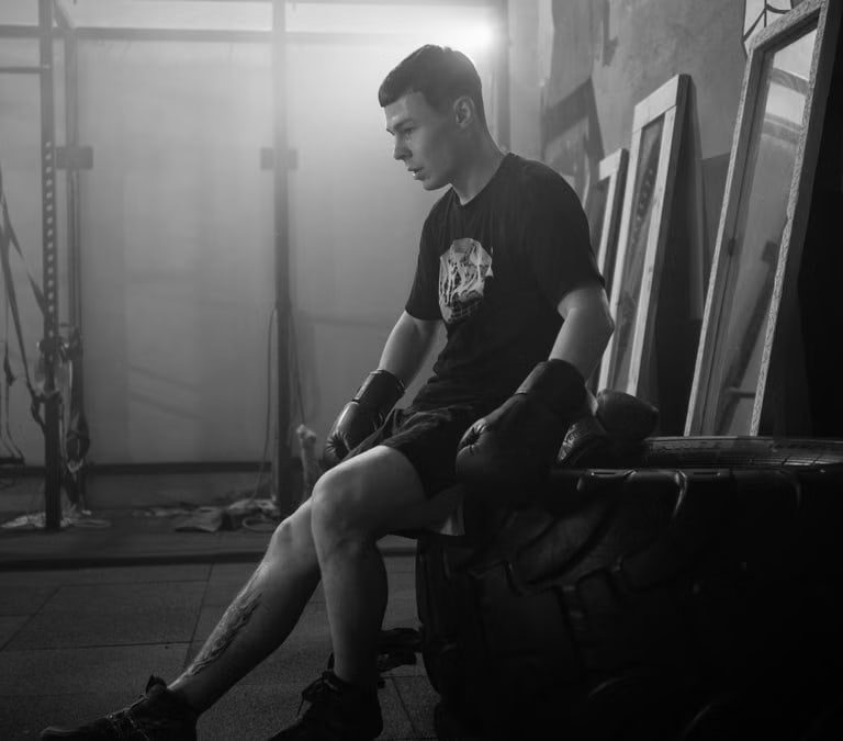 Black and white photo of a boxer resting indoors, showcasing mood and fitness.